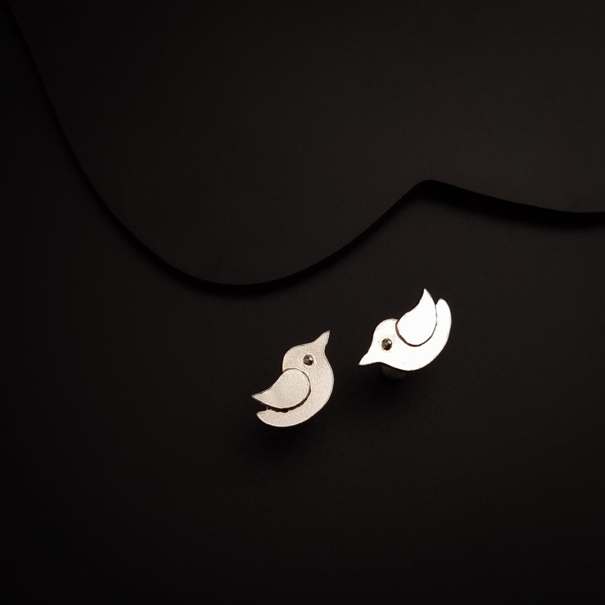 a pair of bird earrings sitting on top of a black surface