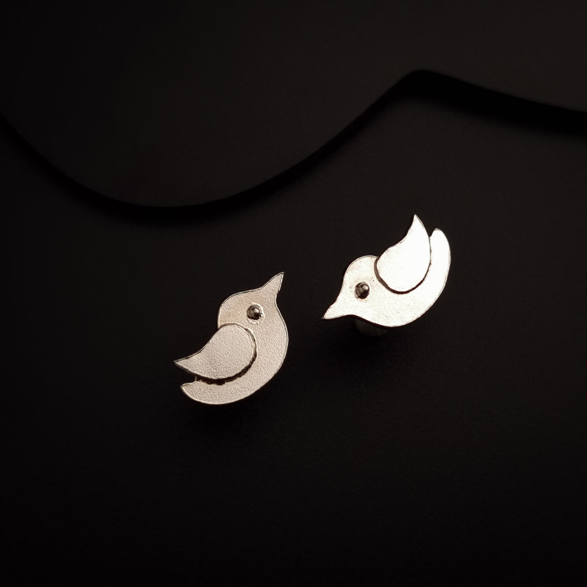 a pair of bird earrings sitting on top of a black surface