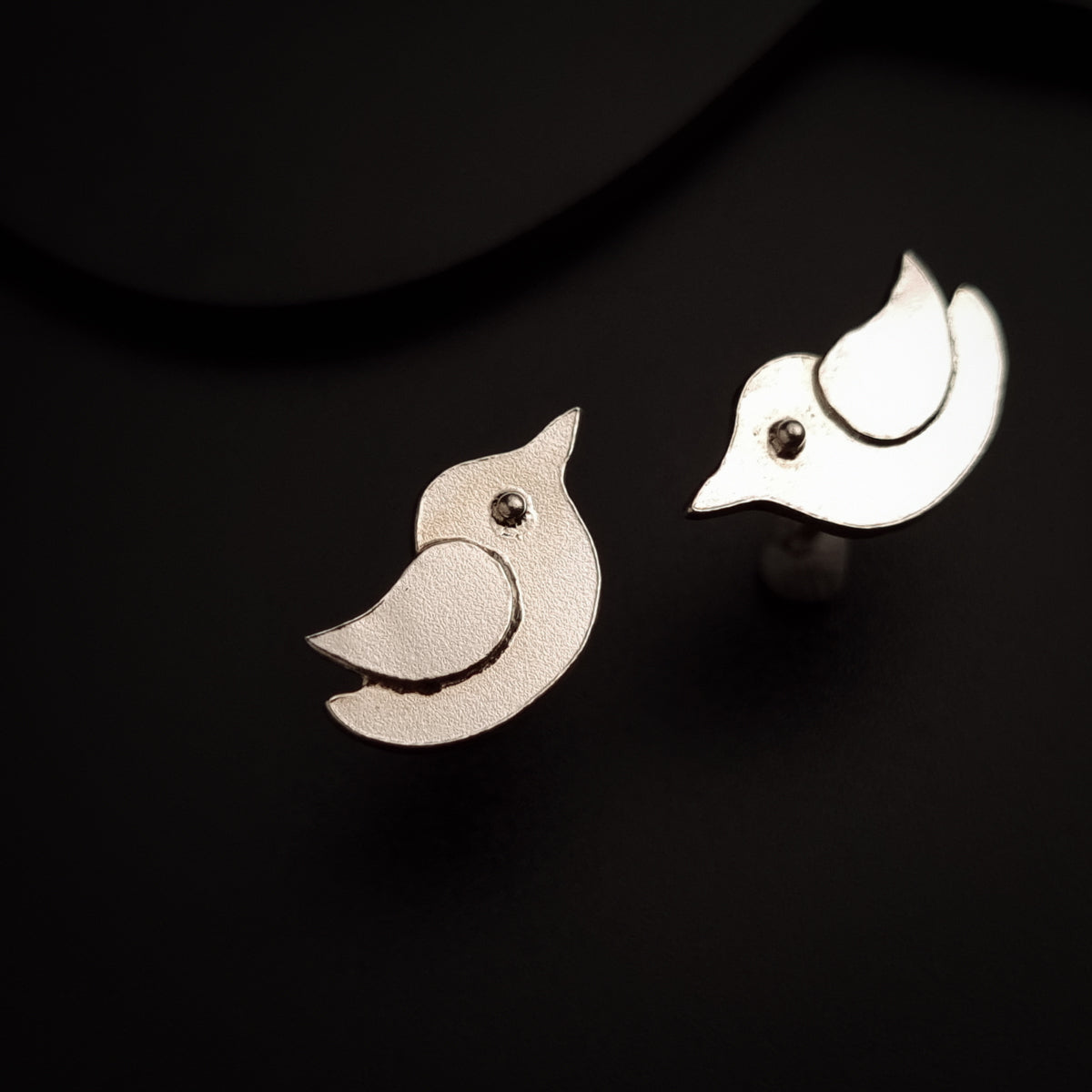 a pair of bird shaped earrings sitting on top of a table