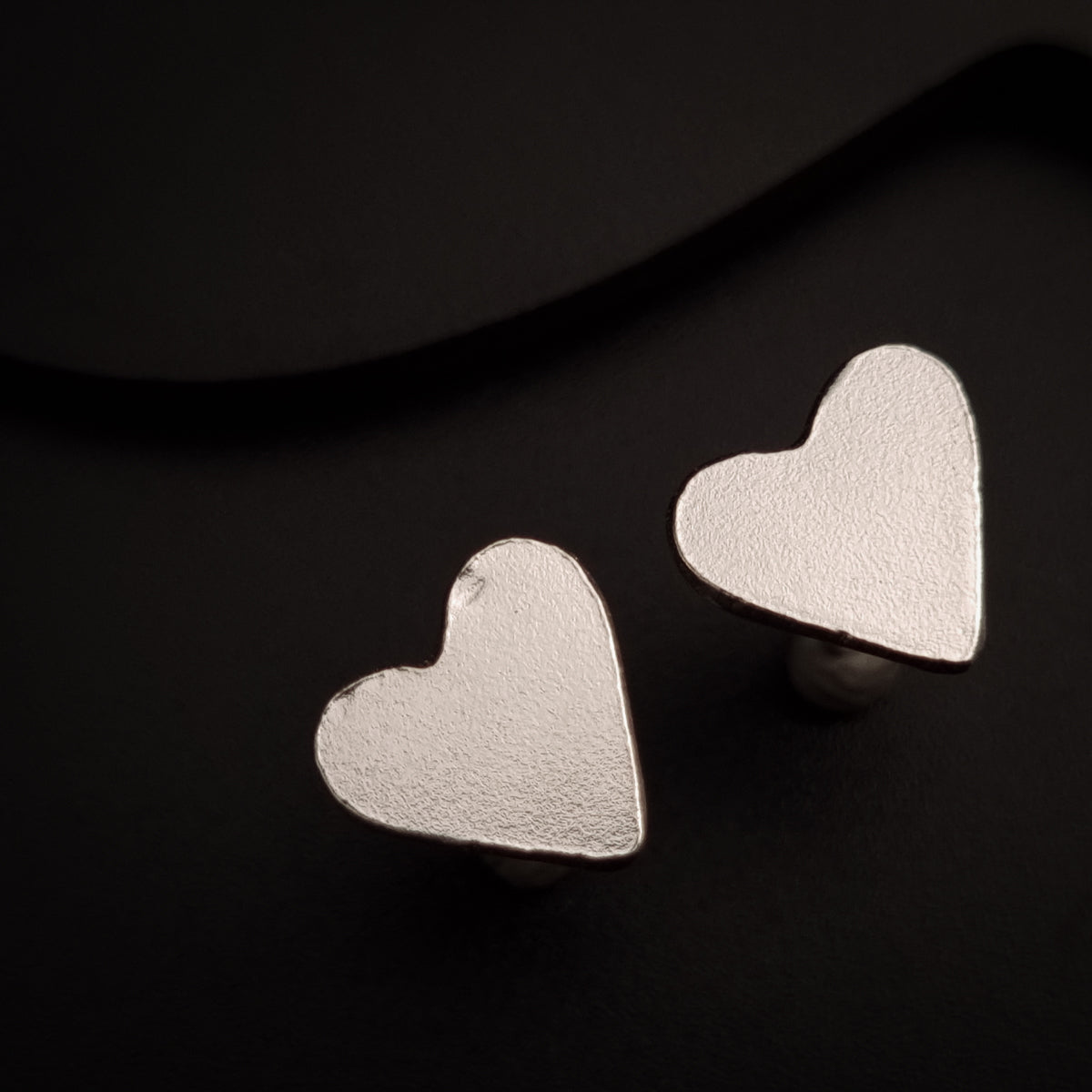 a pair of heart shaped earrings on a black surface