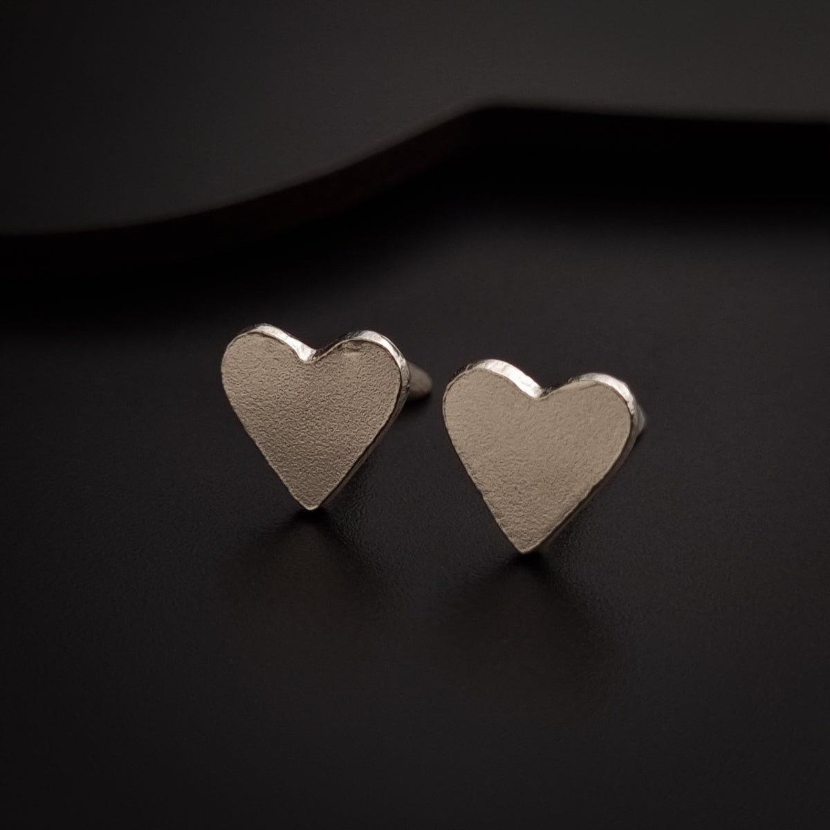 a pair of silver heart earrings on a black surface