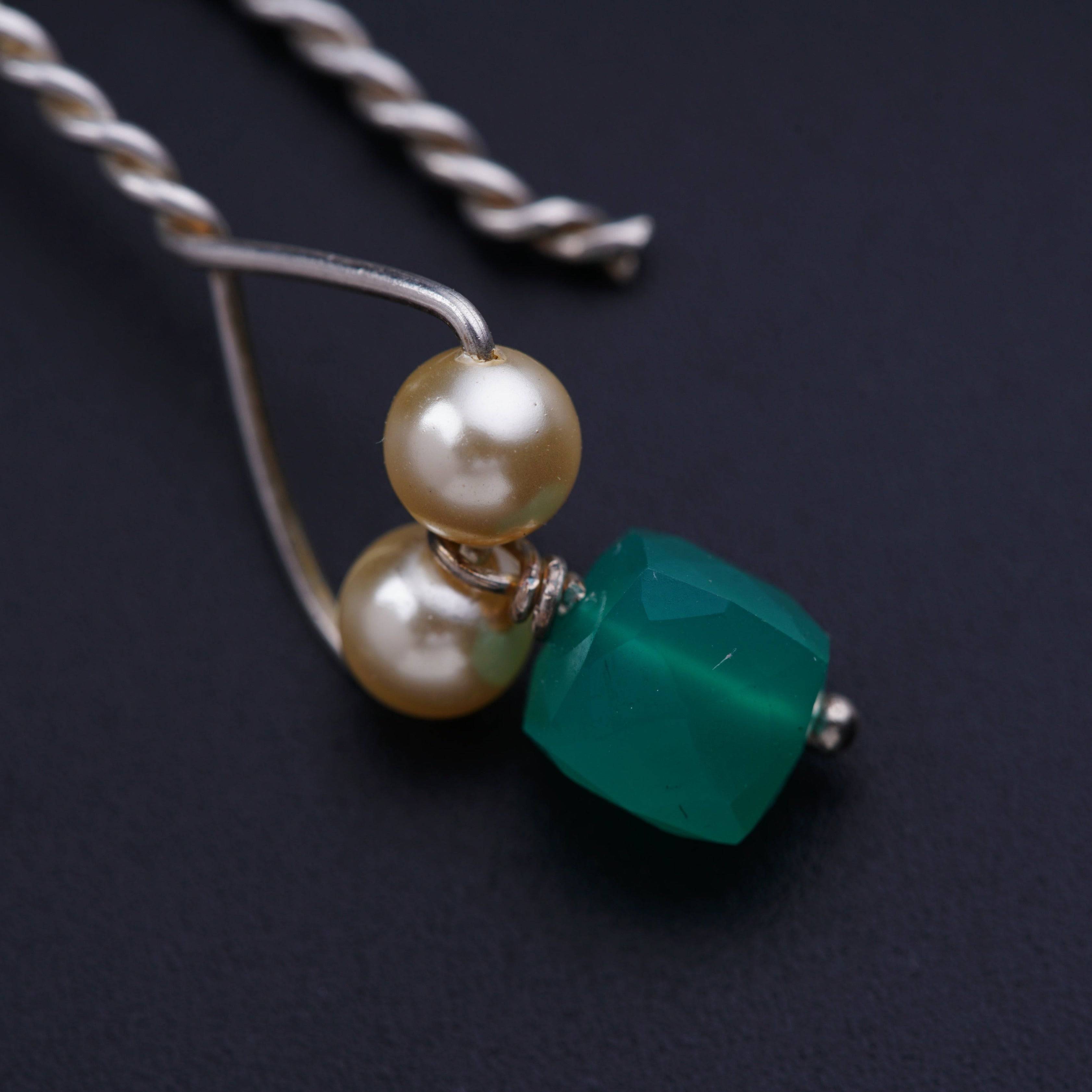 a pair of pearls and a green bead on a necklace