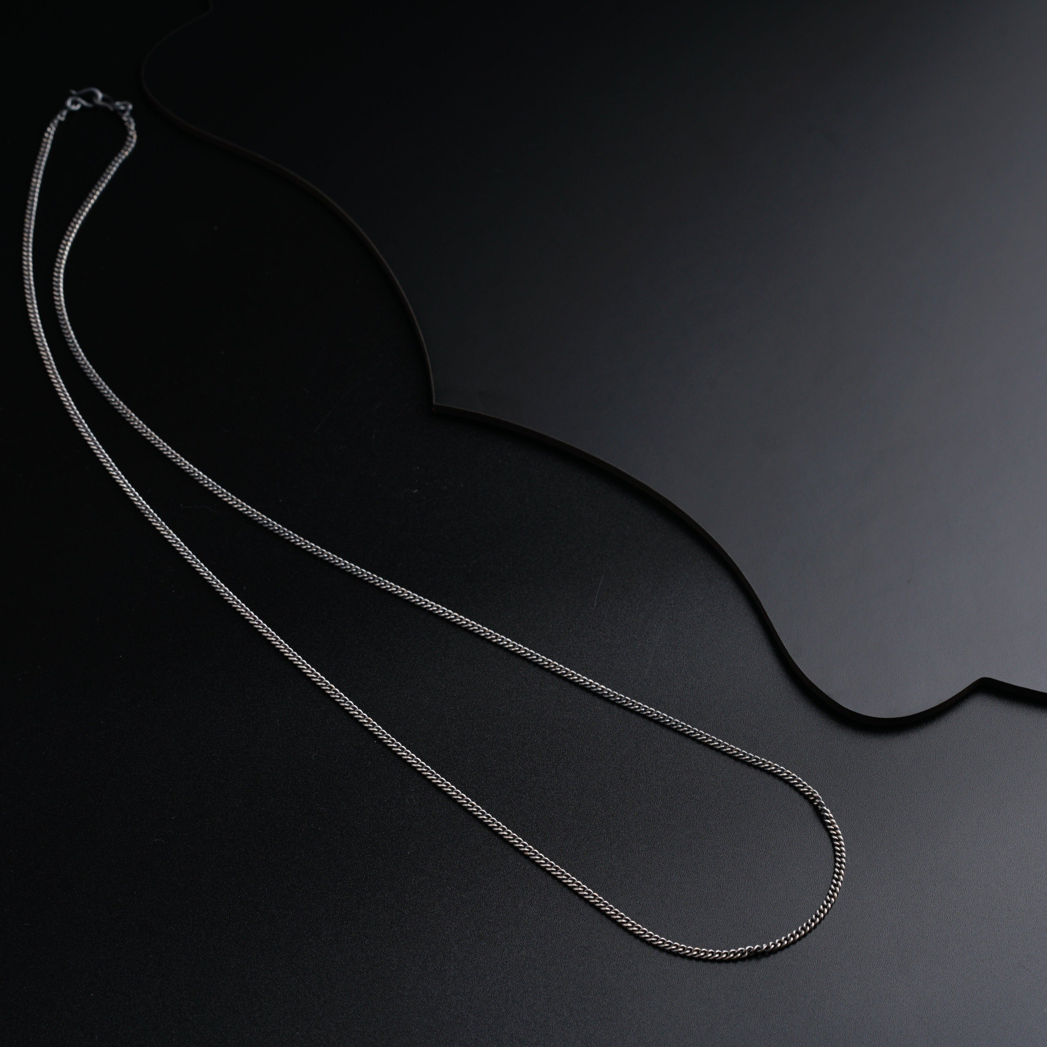 a silver necklace with a chain on a black surface