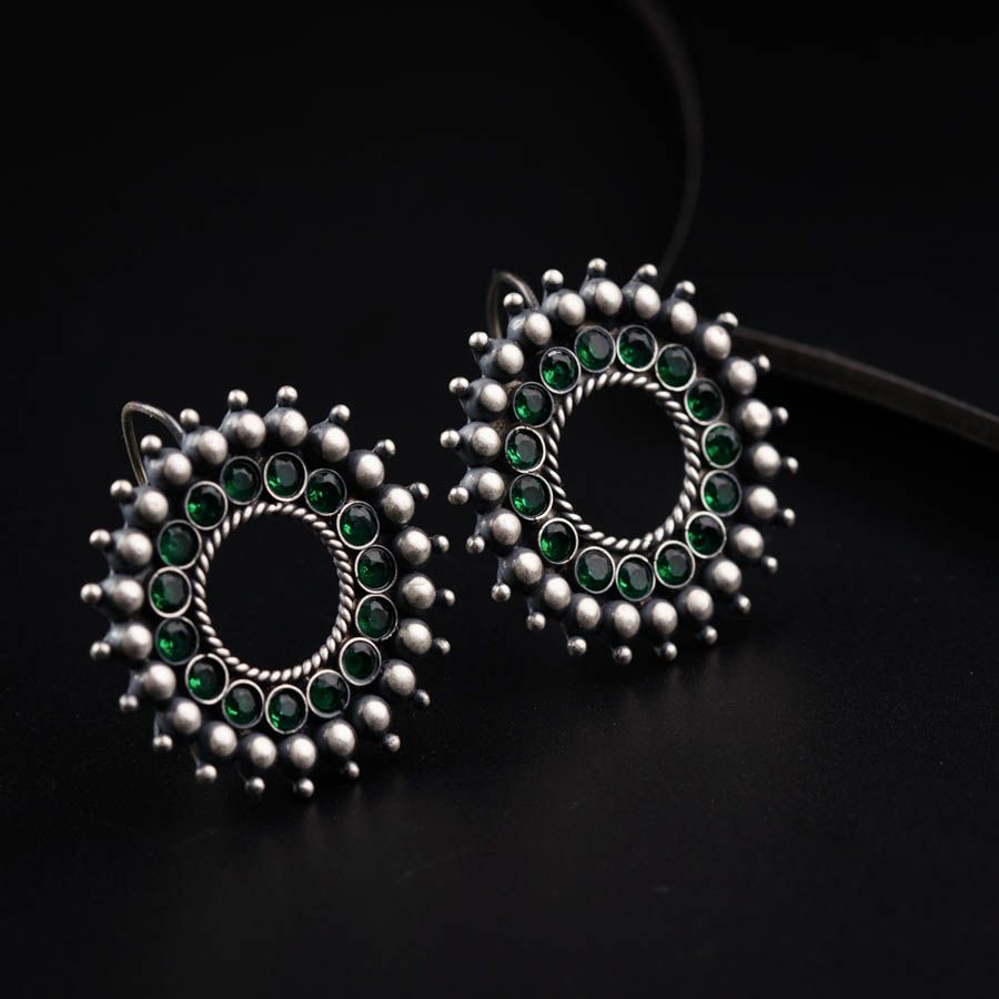 a pair of green and silver earrings on a black surface