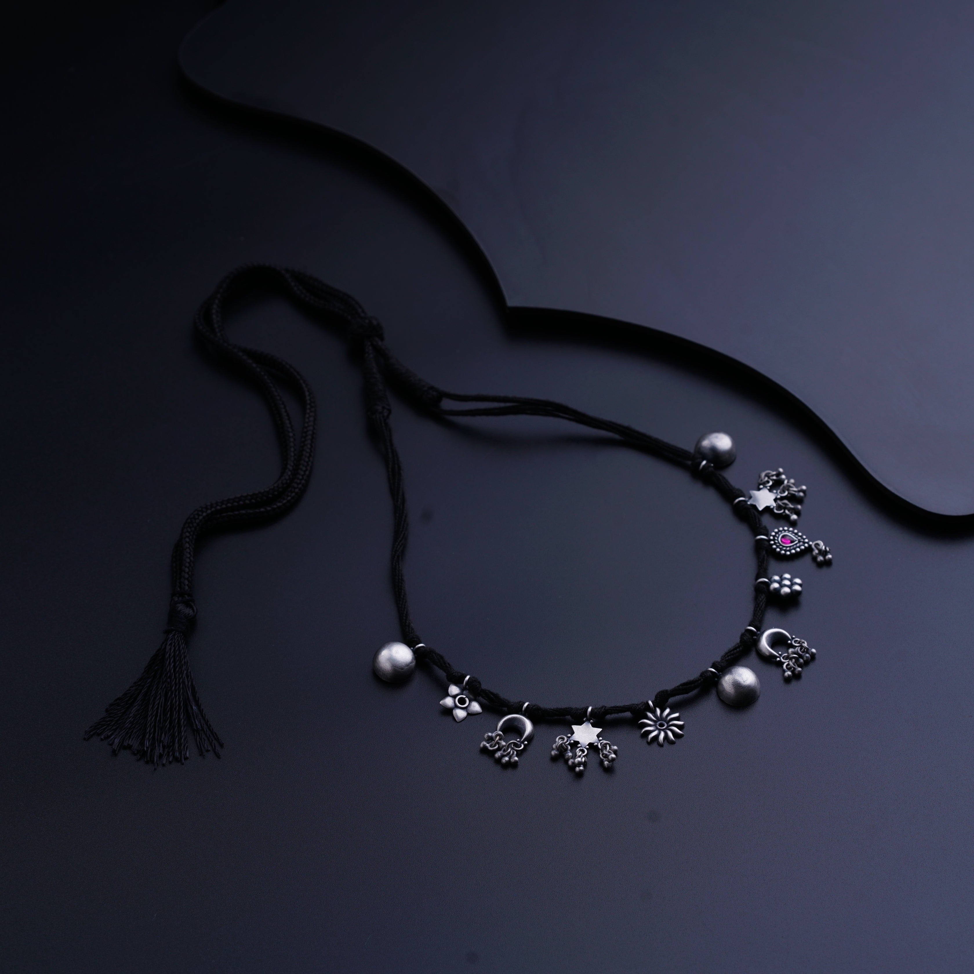 a black necklace with a tassel and a flower