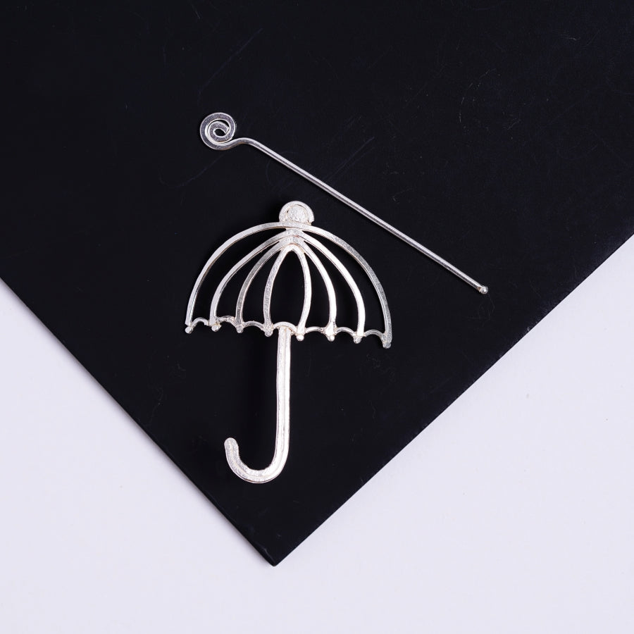 an umbrella shaped brooch sits on top of a black piece of paper