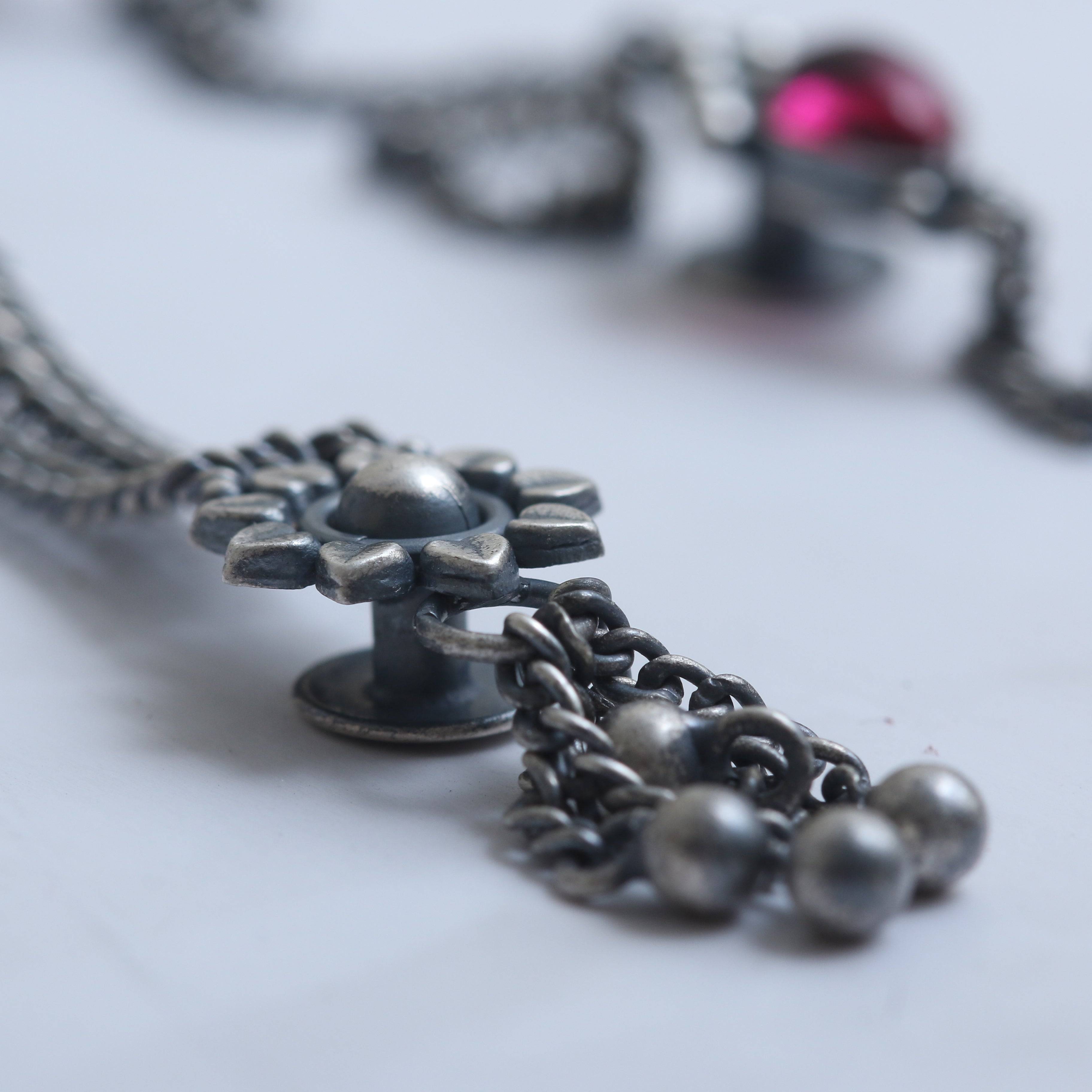 a close up of a chain with a red jewel on it