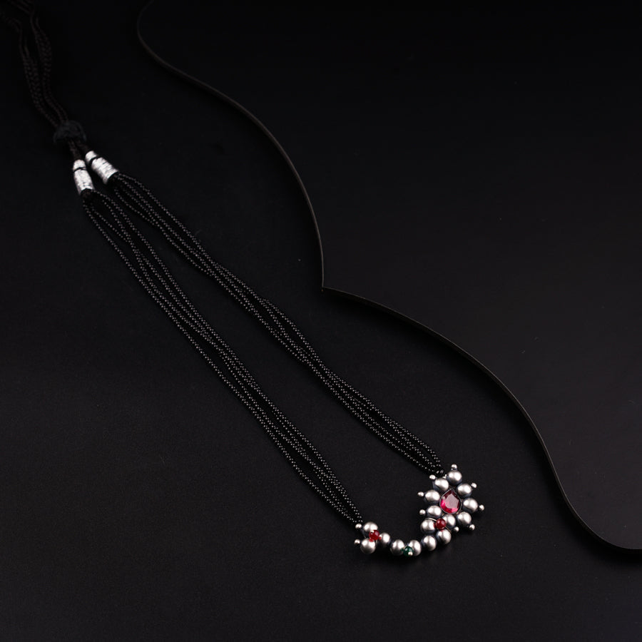 a black necklace with a red and white bead