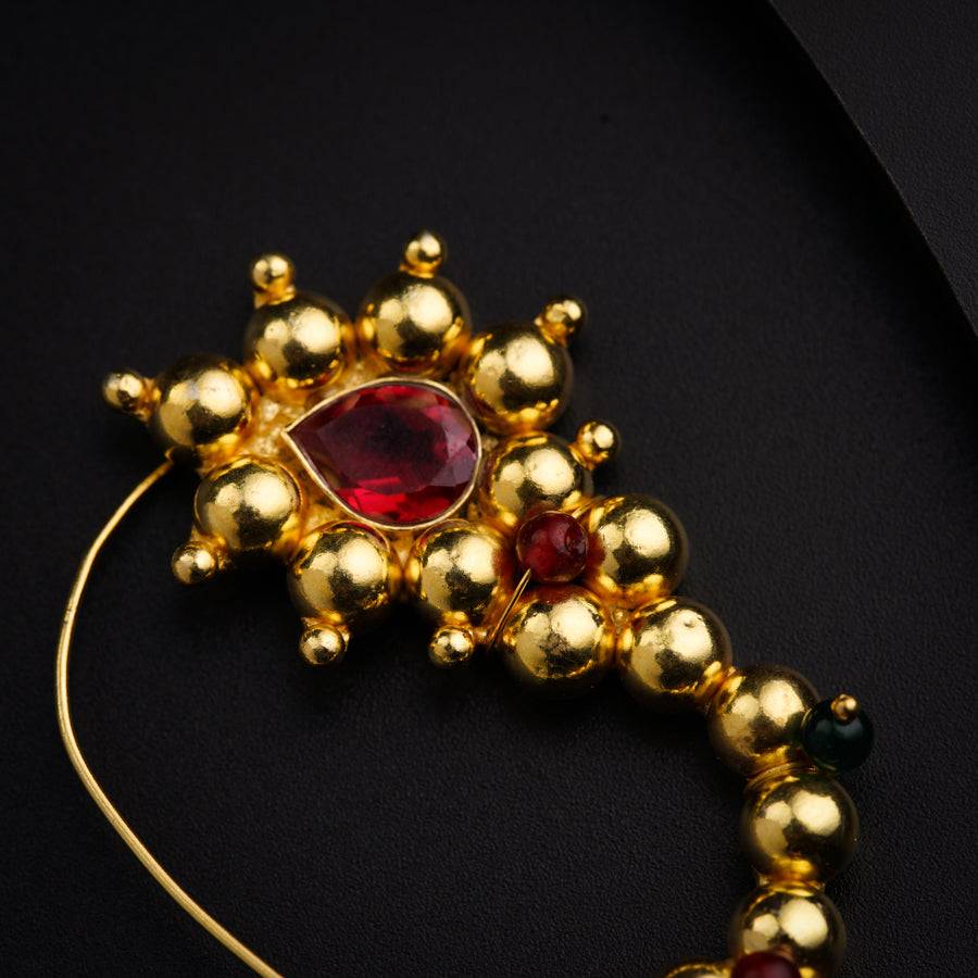 a close up of a gold necklace with a red stone