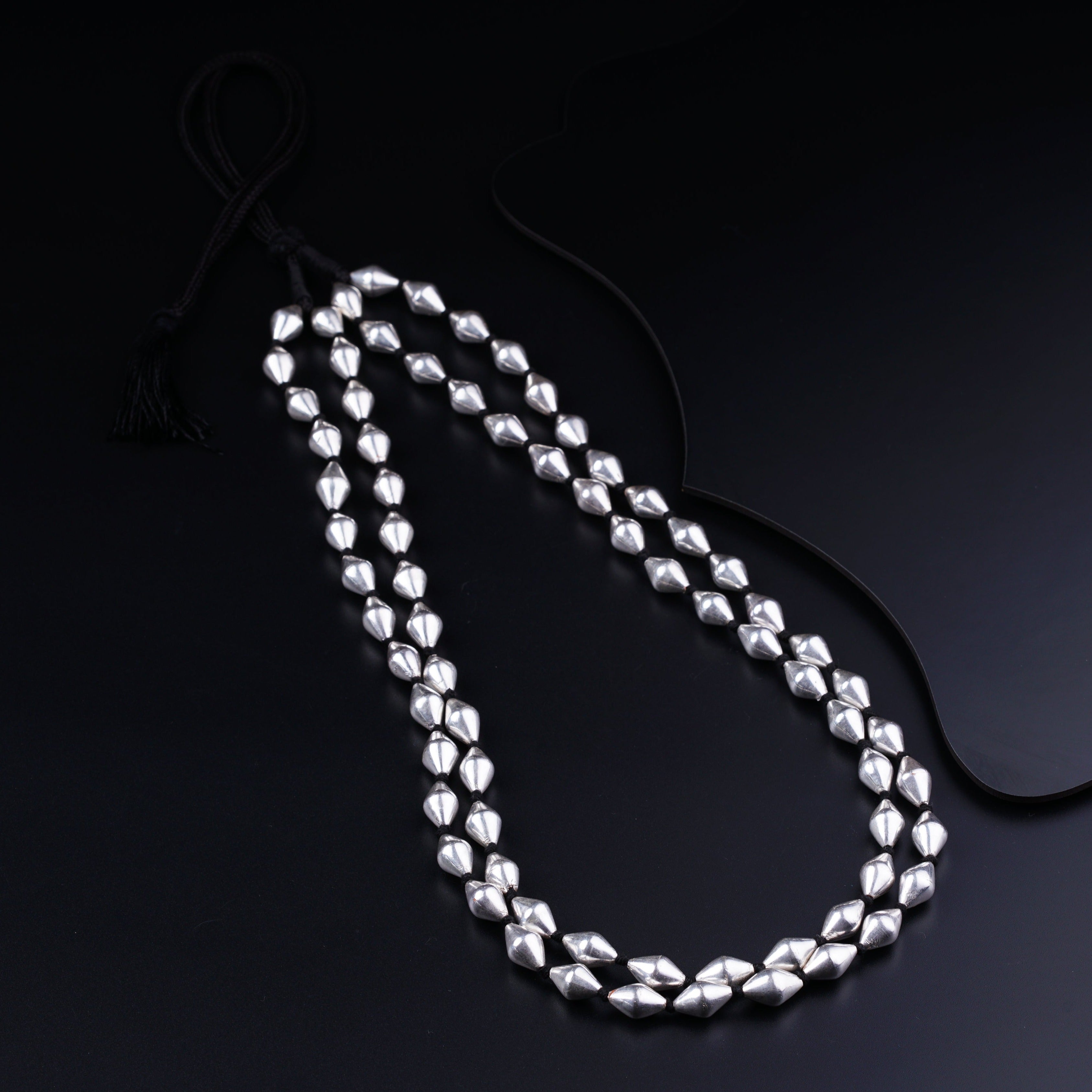 a long necklace with silver beads on a black background