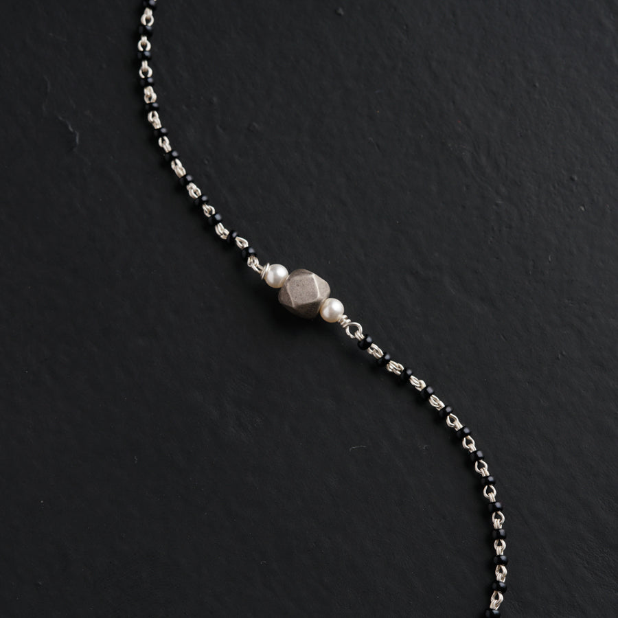 a silver beaded necklace on a black surface
