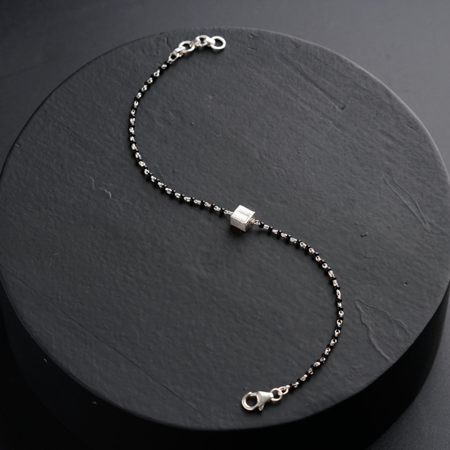 a silver beaded bracelet on a black surface