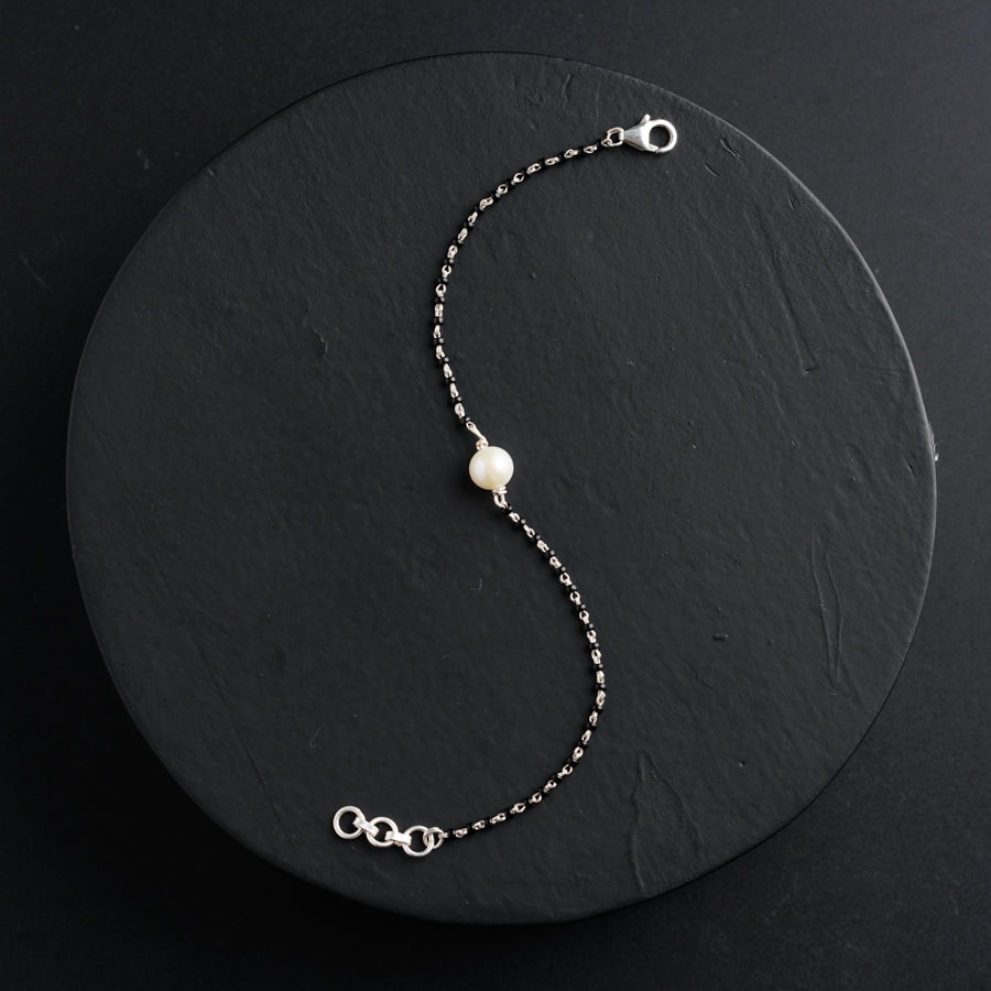 a white pearl and silver chain bracelet on a black background