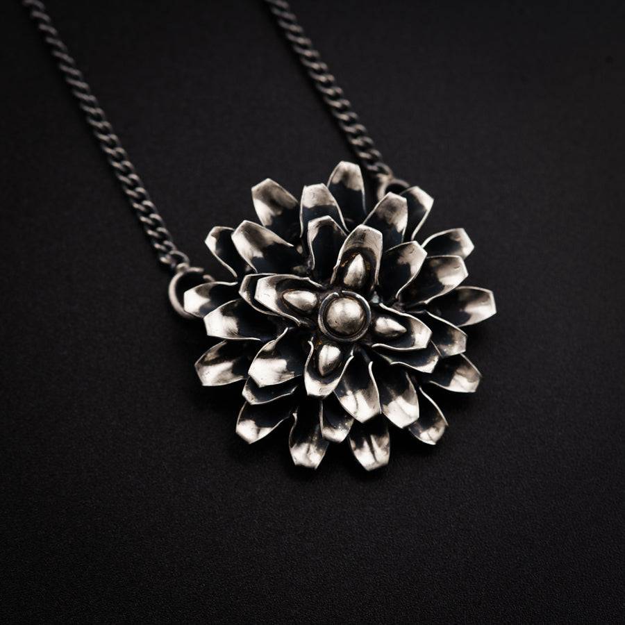 a silver flower necklace on a black background
