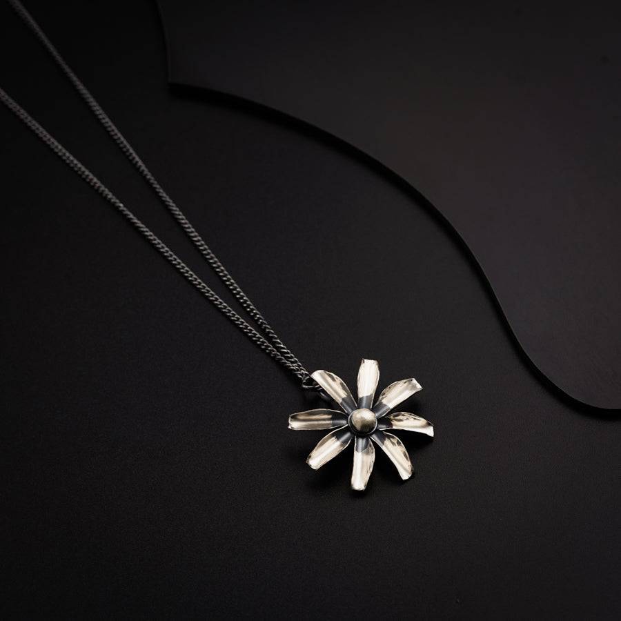 a silver necklace with a flower on a black background
