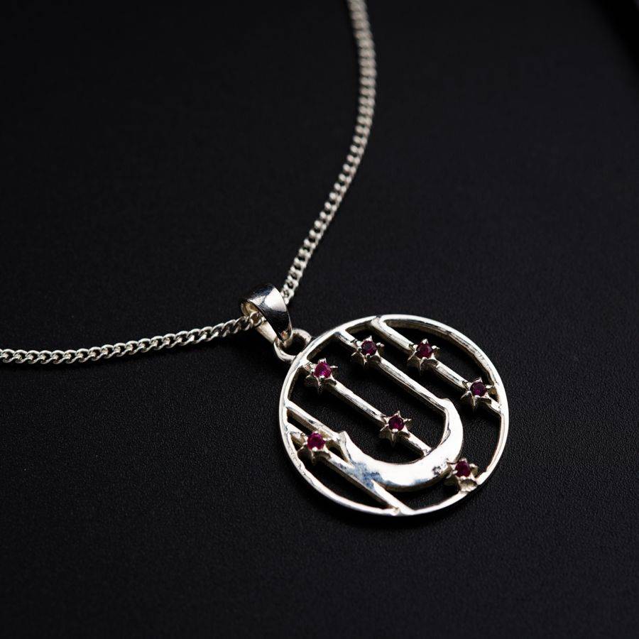 a silver necklace with a silver circle and a red bead on it