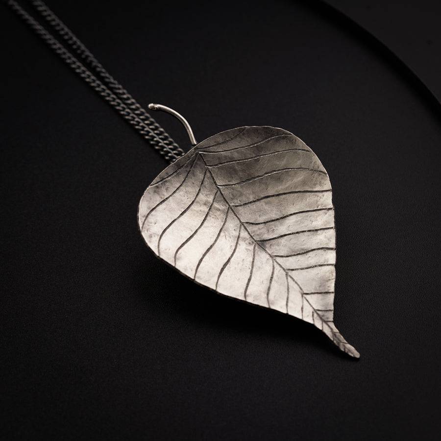 a silver leaf pendant on a black background