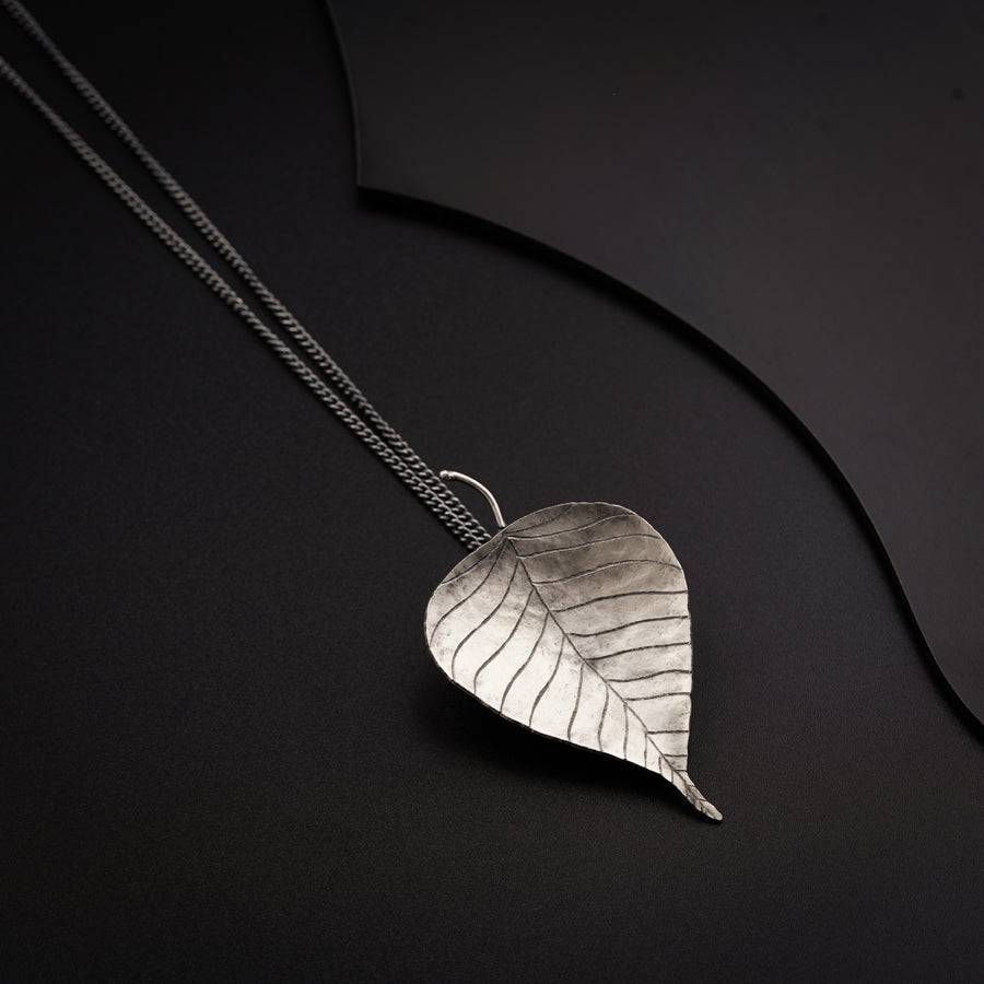a silver leaf necklace on a black background