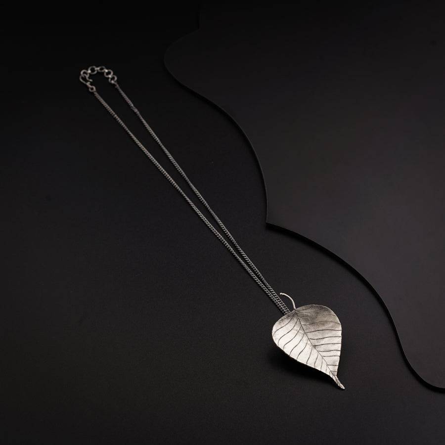 a silver leaf necklace on a black background