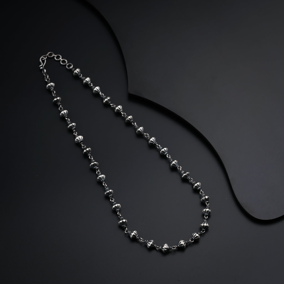 a silver beaded necklace on a black surface