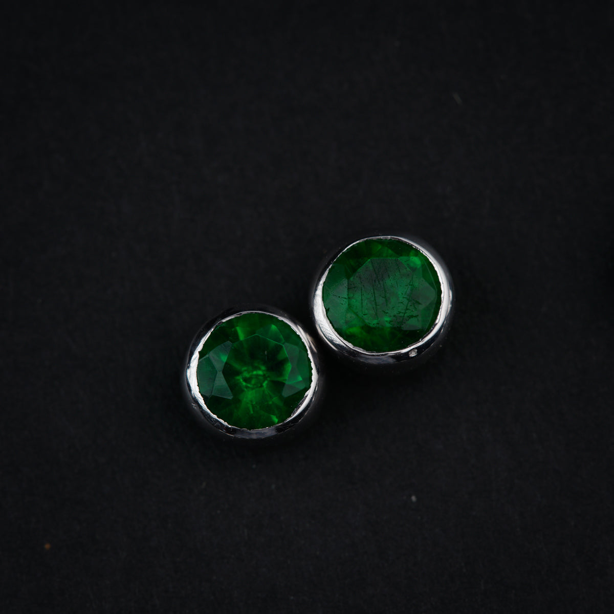 a pair of green earrings sitting on top of a black surface