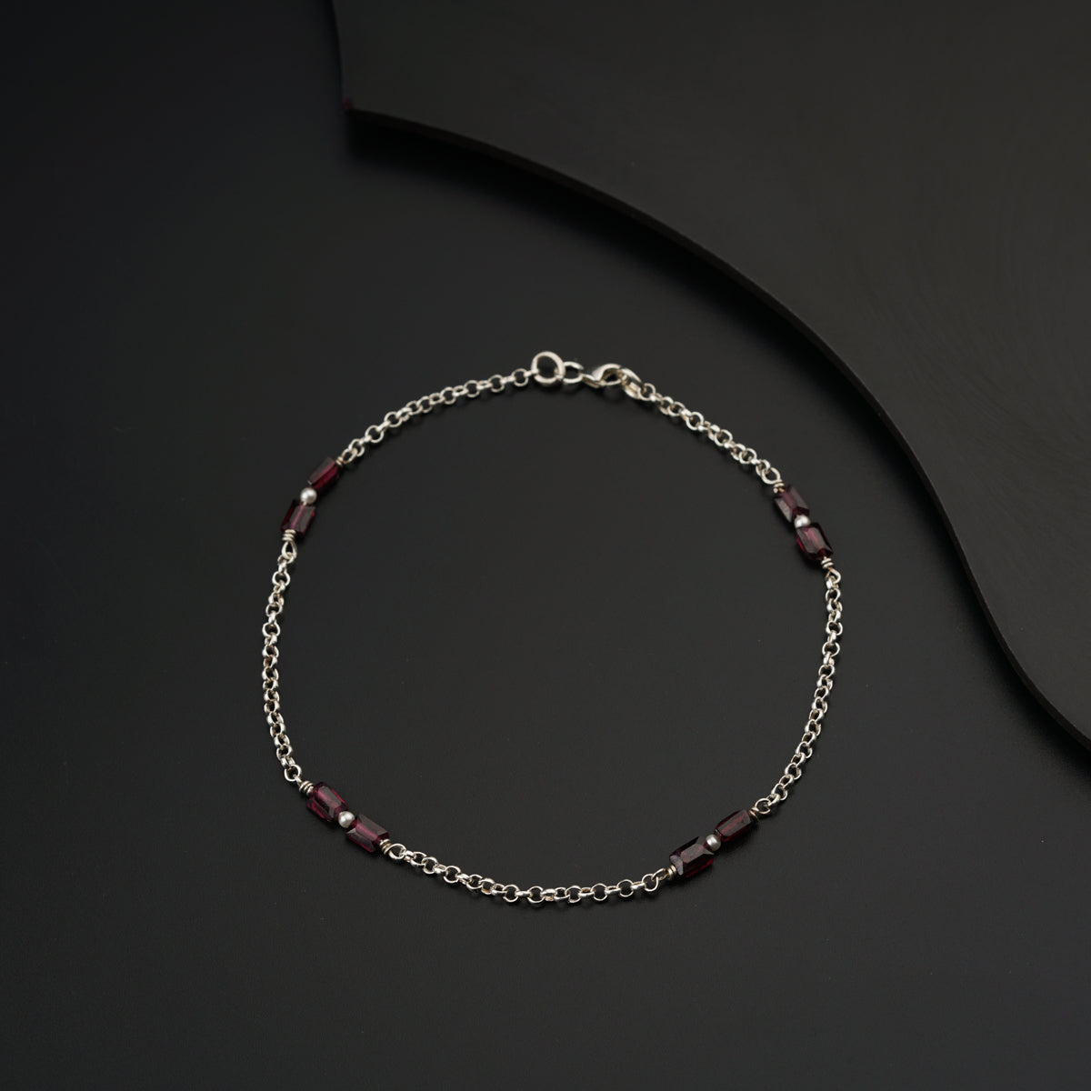 a silver bracelet with a red bead on a black surface