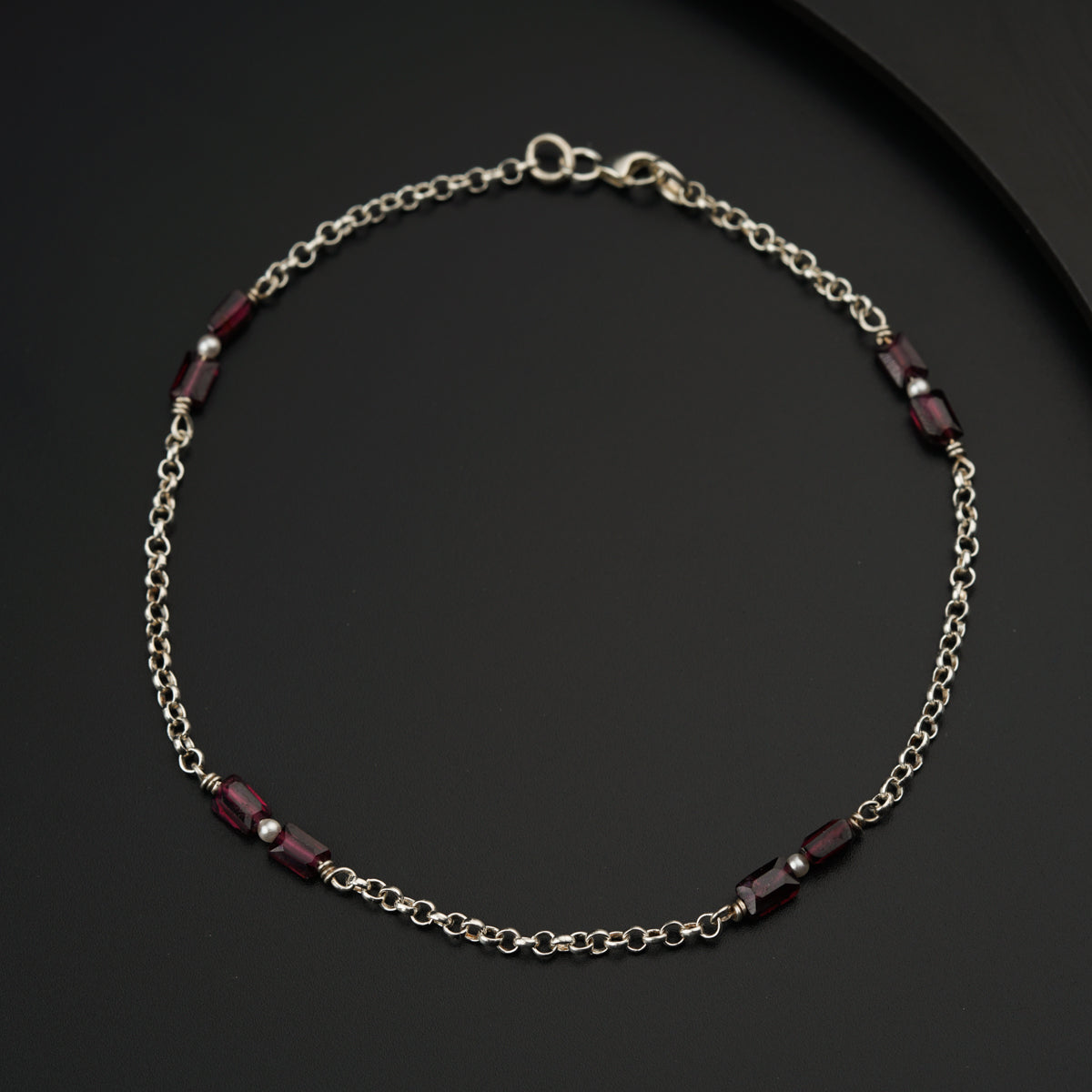 a silver chain with a red bead on it