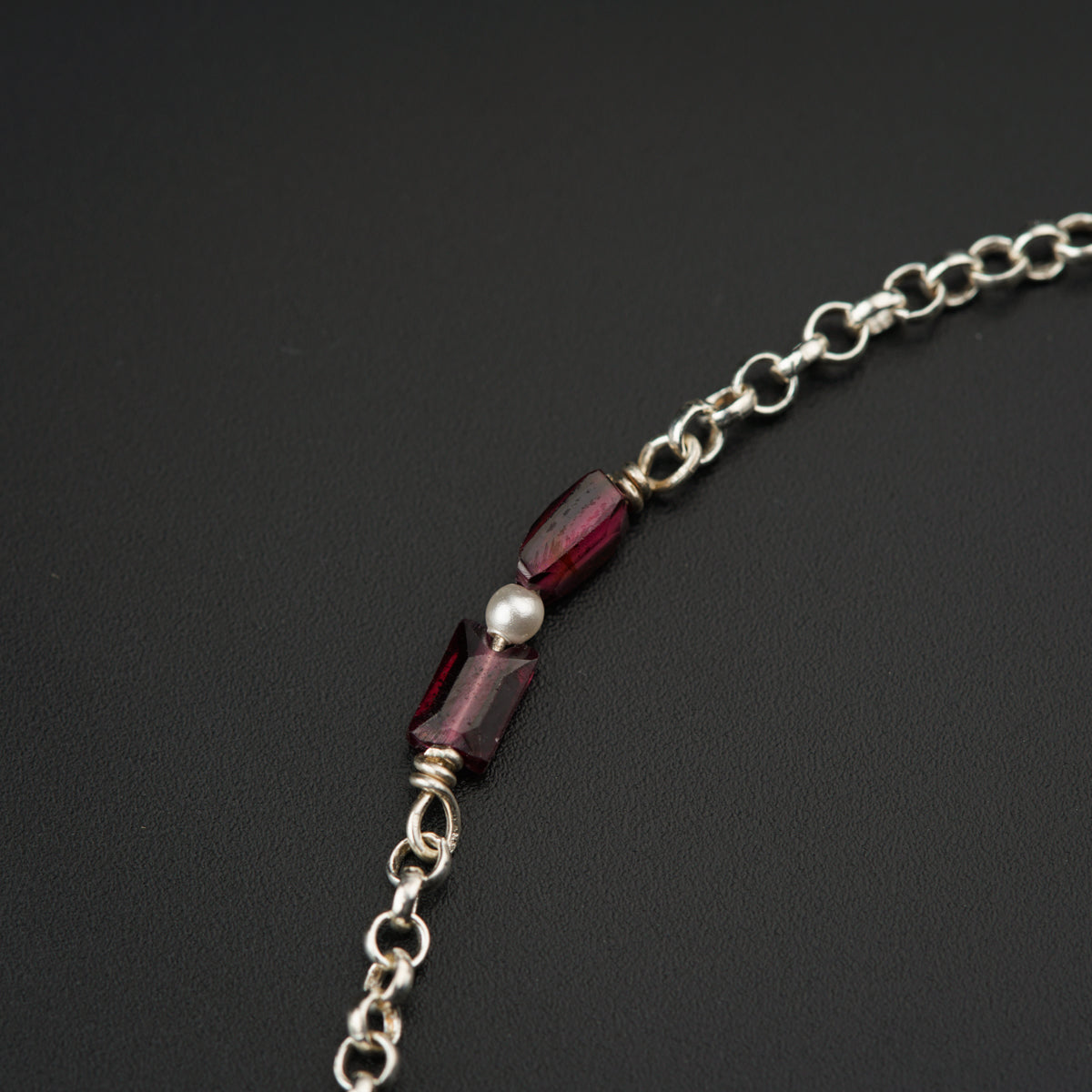 a silver chain with a red glass bead on it