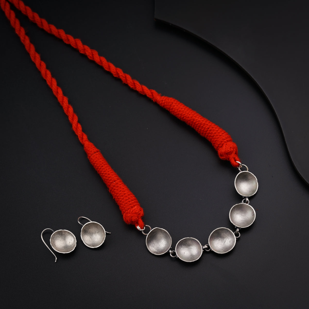 a necklace and earring with a red cord on a black surface