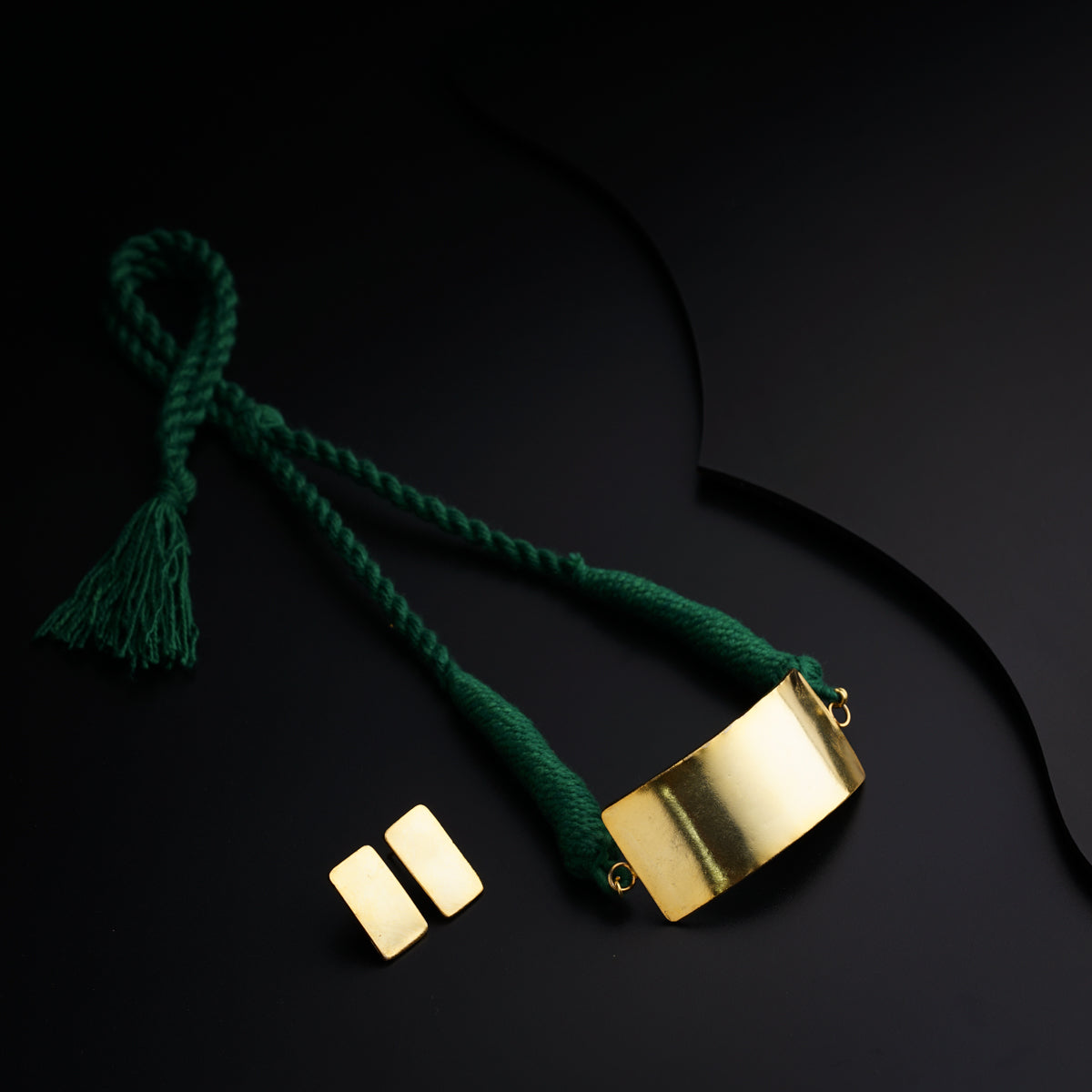 a gold necklace with a green tassel on a black background