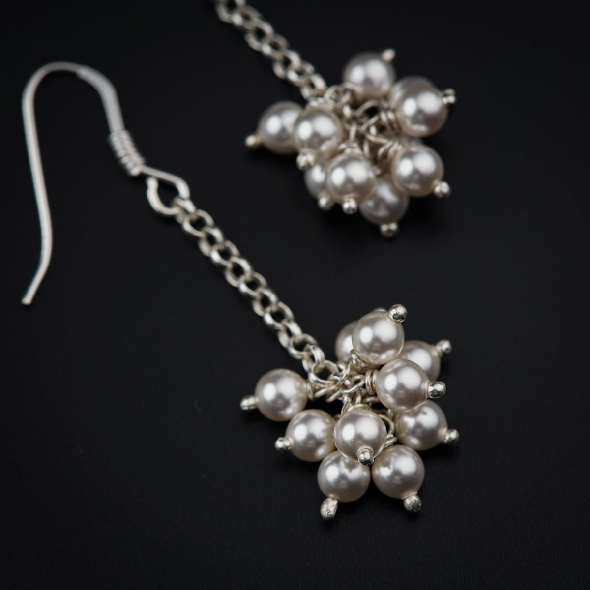 a pair of silver and pearl earrings on a black background
