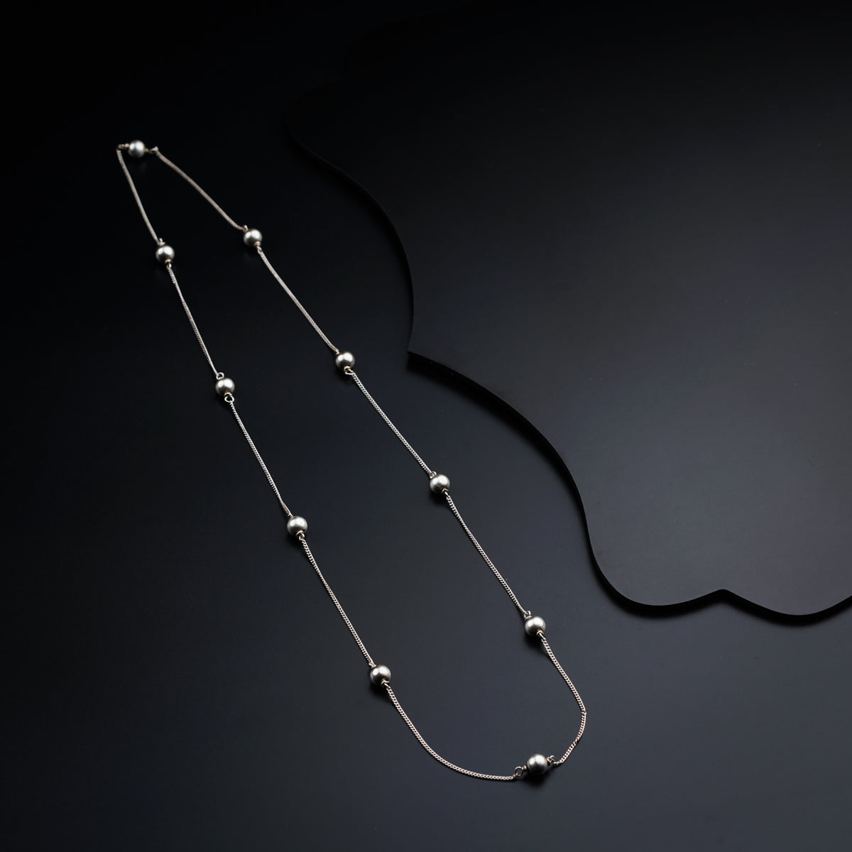 a silver necklace with beads on a black background