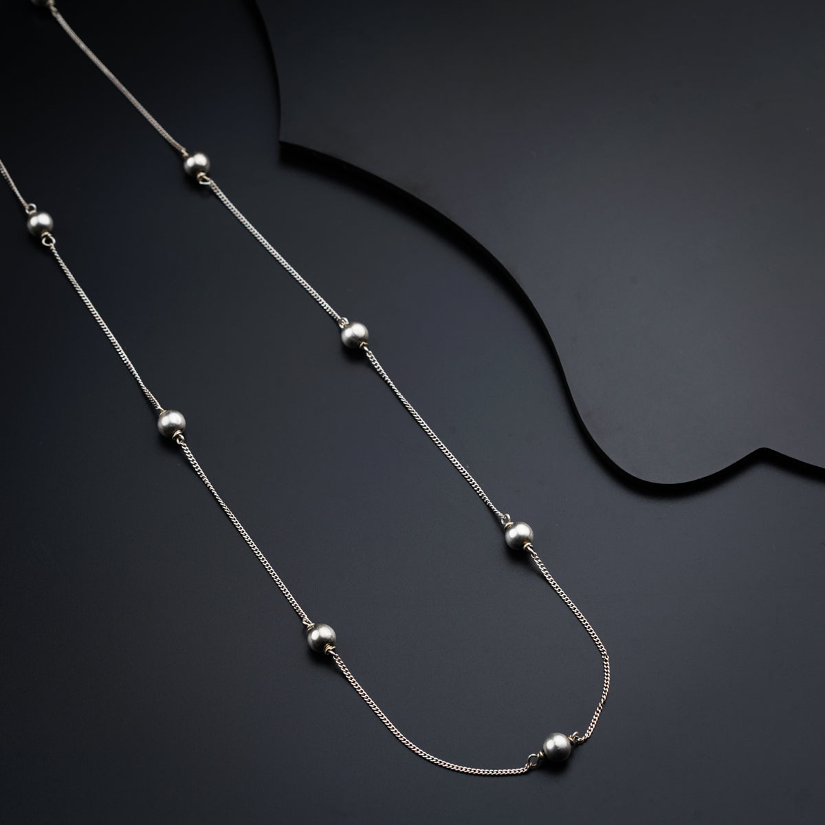 a silver necklace with balls on a black background