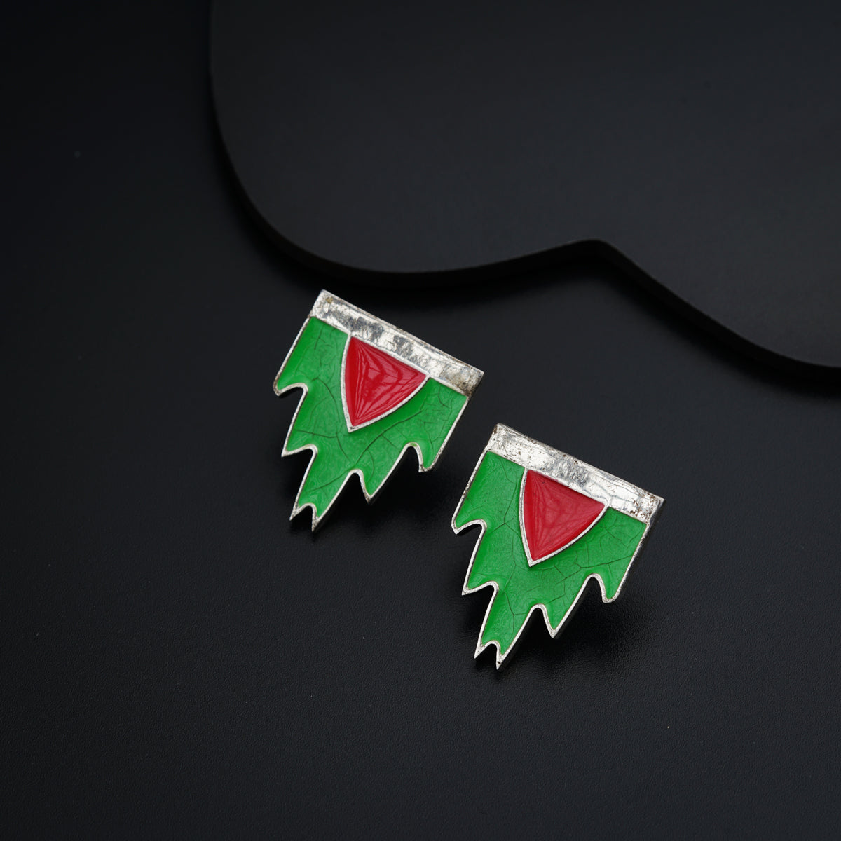 a pair of green and red earrings on a black surface