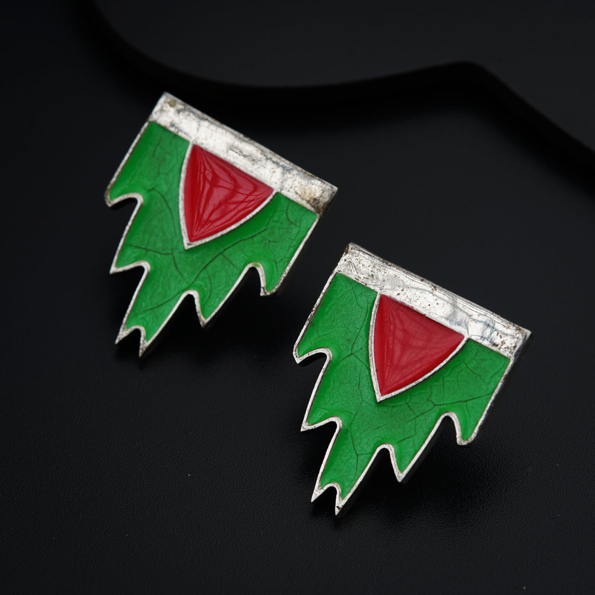 a pair of green and red earrings on a black surface