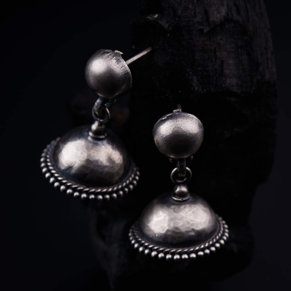 a pair of silver earrings sitting on top of a piece of wood