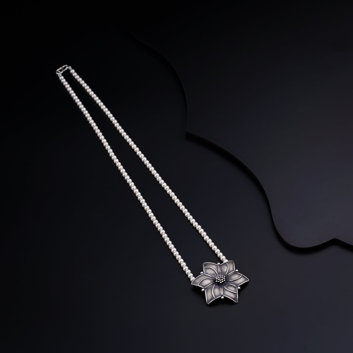 a necklace with a flower on a black background