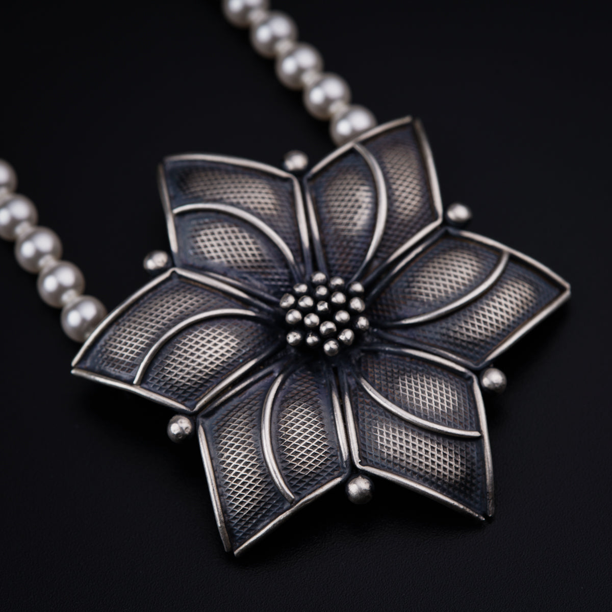 a necklace with a flower and pearls on a black background