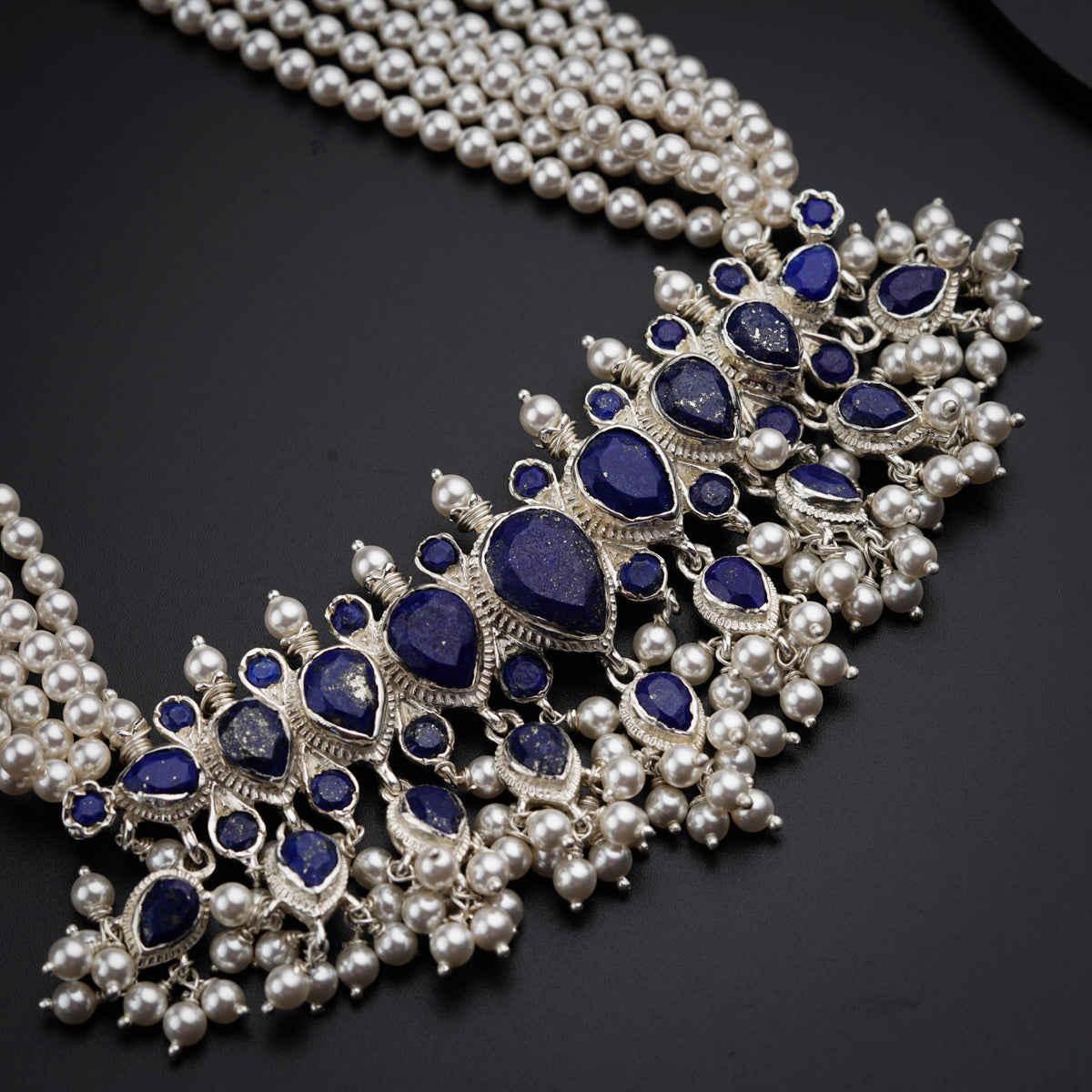 a necklace with blue stones and pearls on a black surface