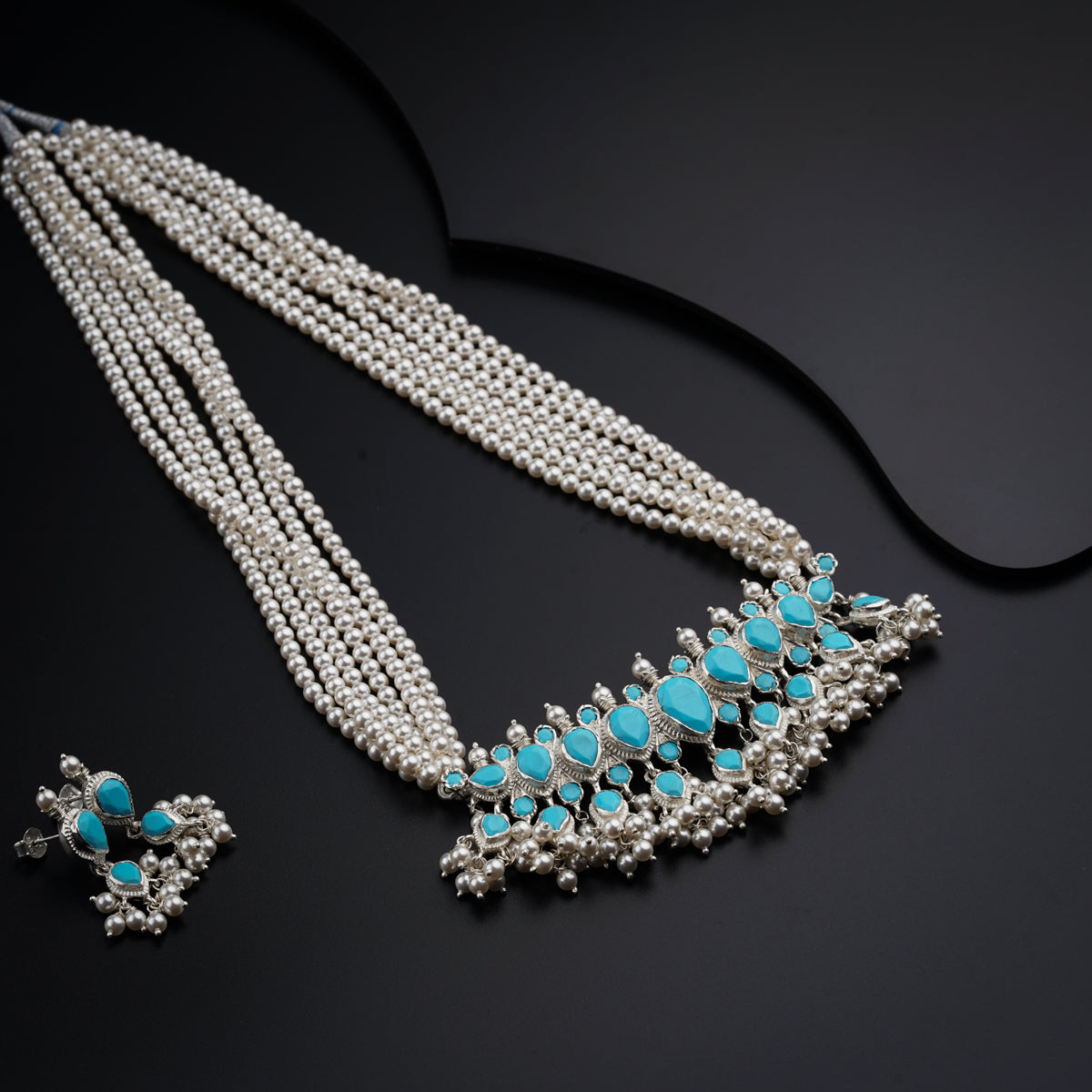 a necklace with pearls and turquoise stones on a black surface