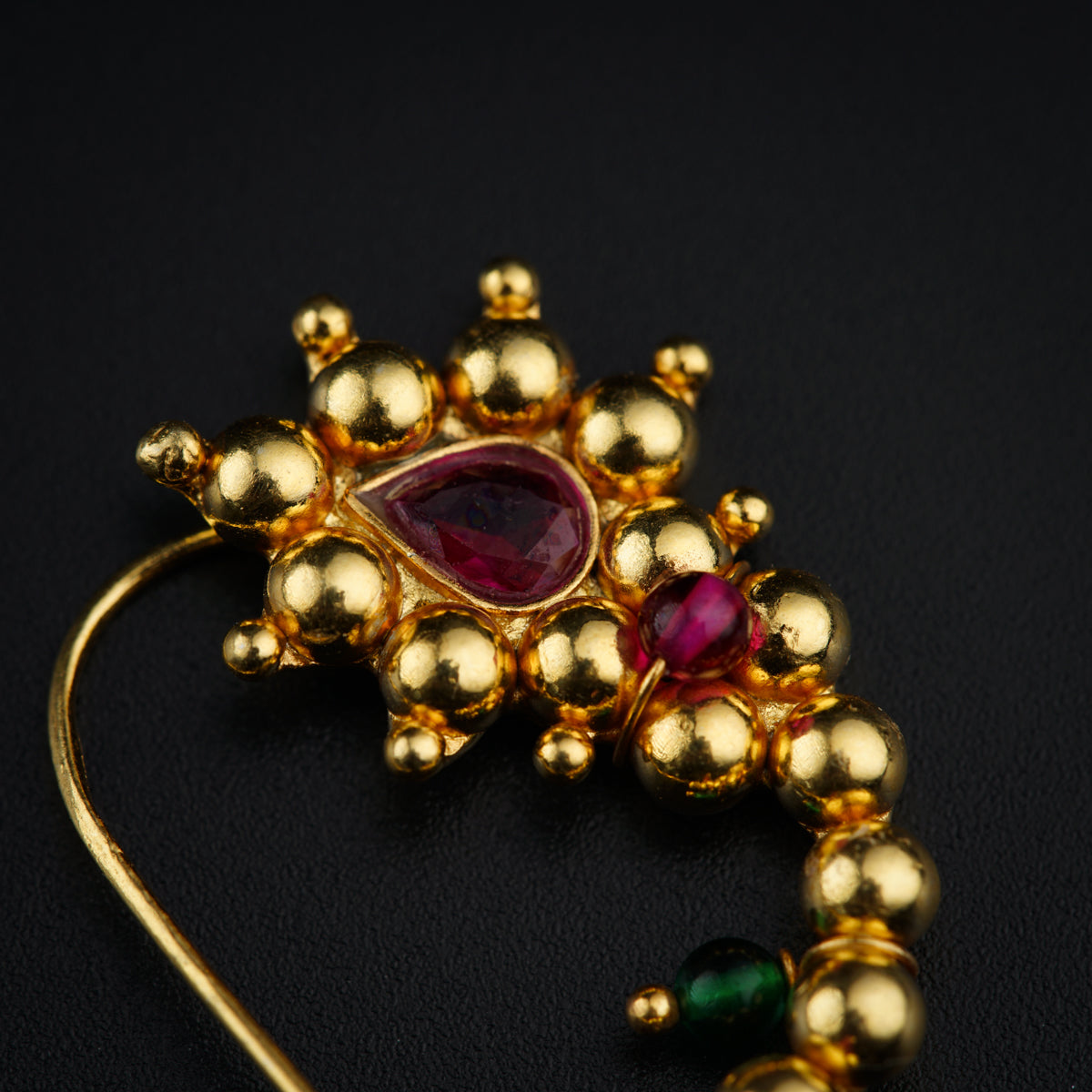 a close up of a gold brooch with a red stone