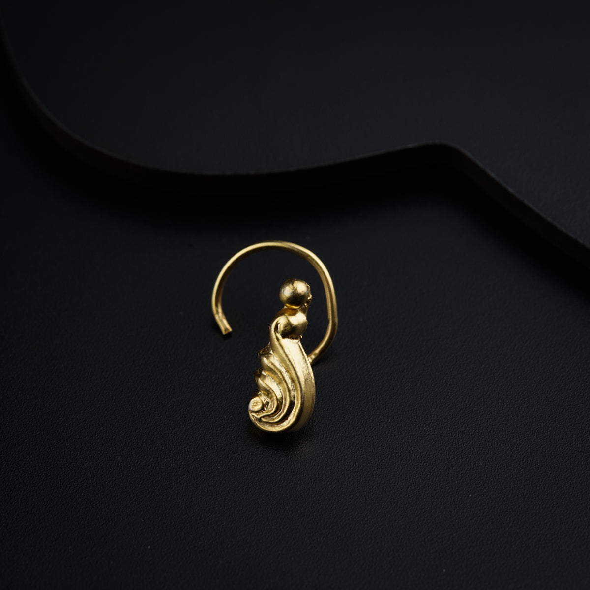 a close up of a gold earring on a black surface
