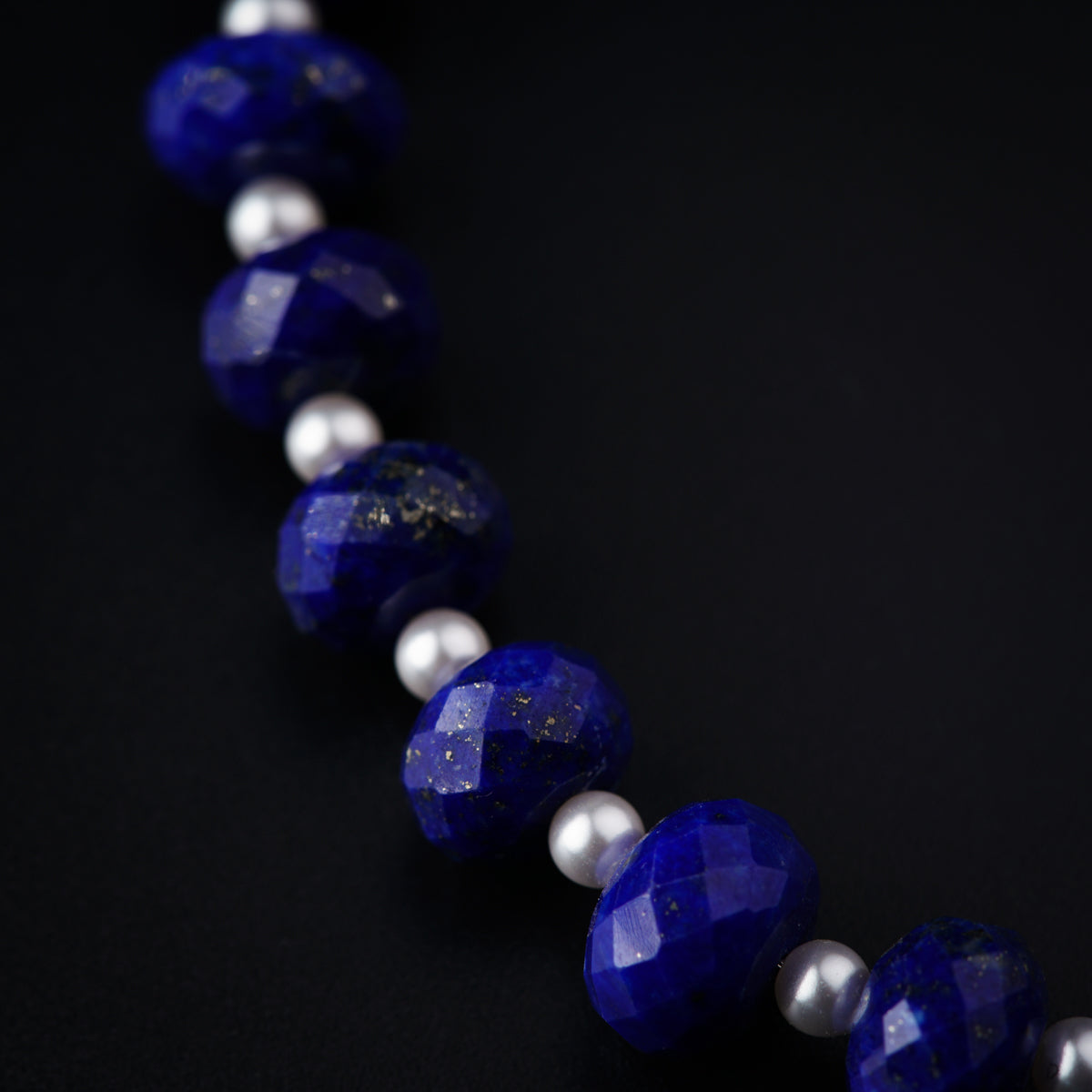 a blue necklace with white pearls on a black background