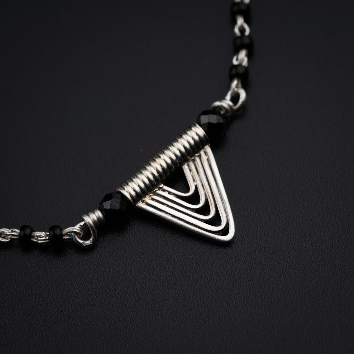a silver triangle necklace on a black background
