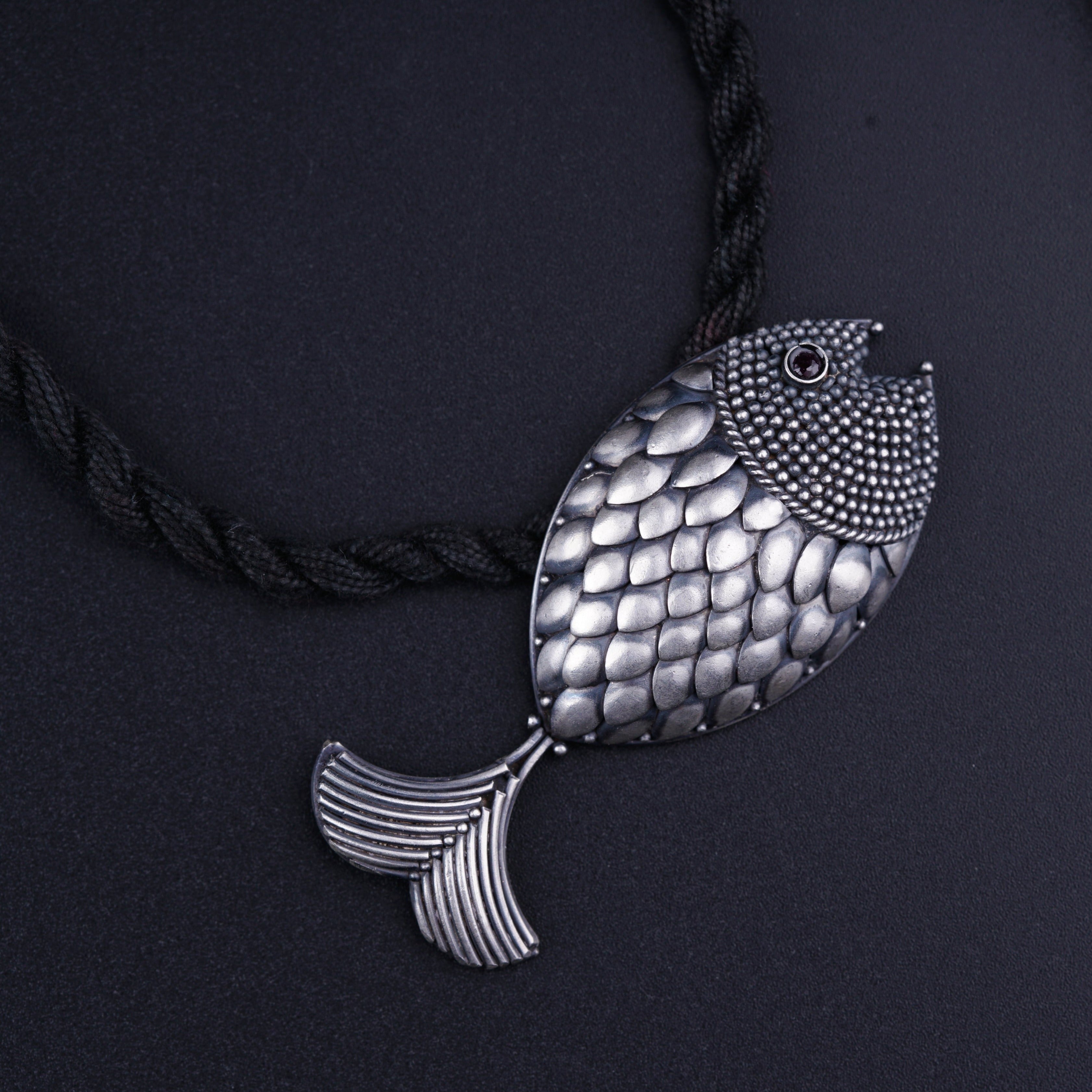 a silver fish pendant on a black cord