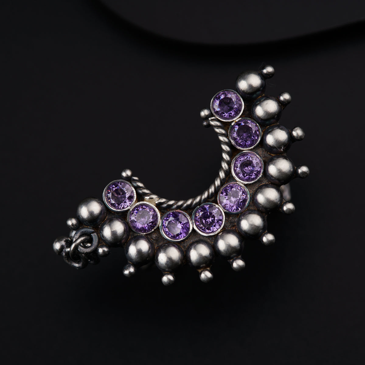 a silver brooch with purple stones on a black background
