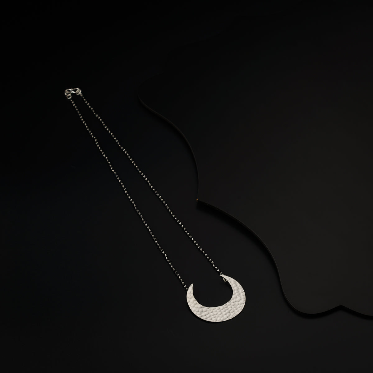 a silver necklace with a crescent on a black background