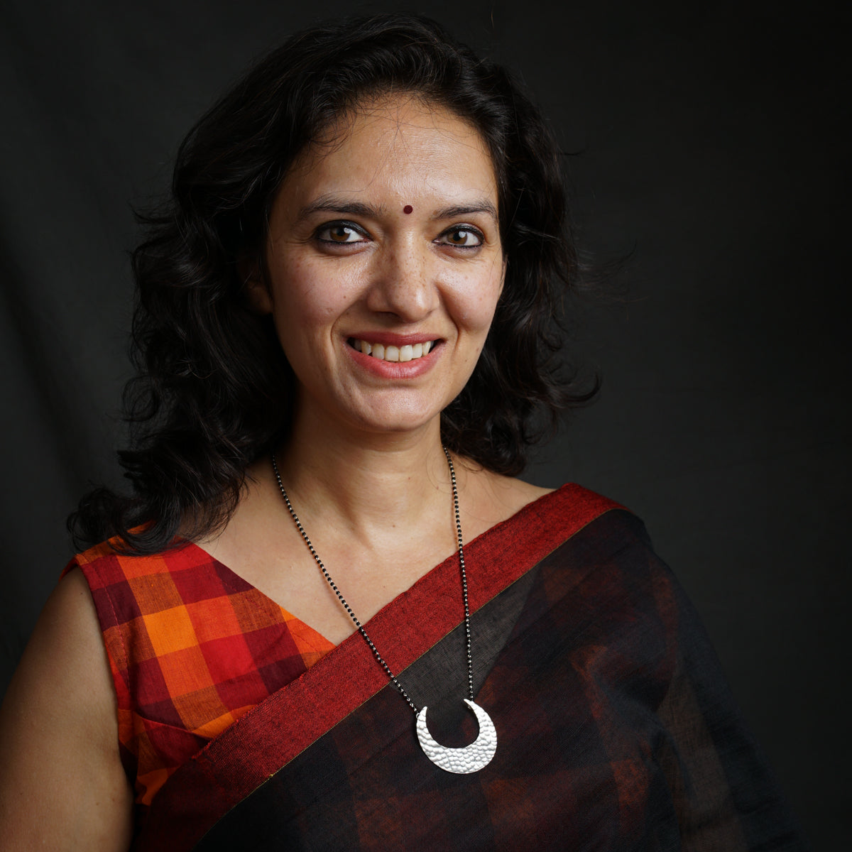 a woman in a red and black sari smiles at the camera