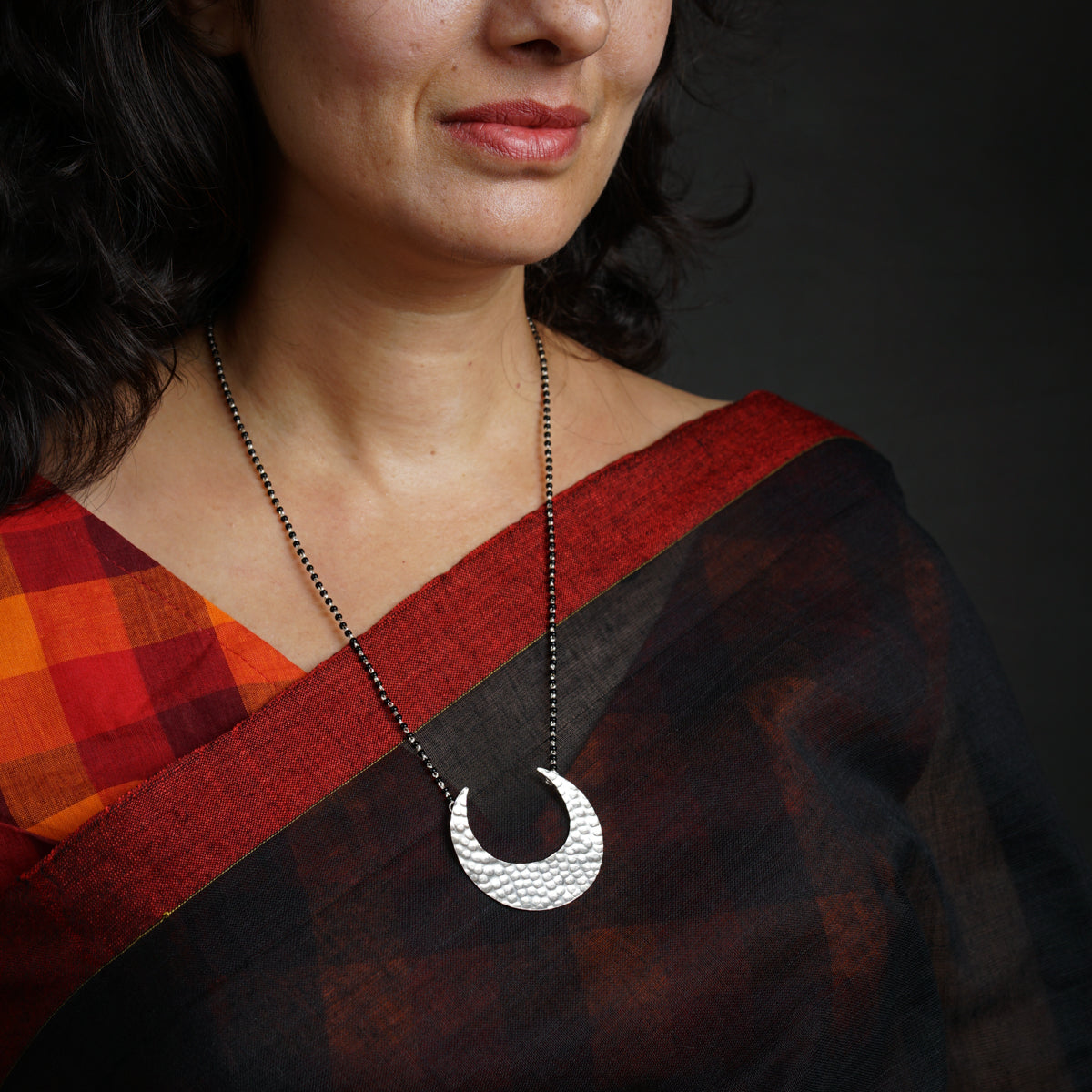 a woman wearing a black and red sari with a crescent pendant