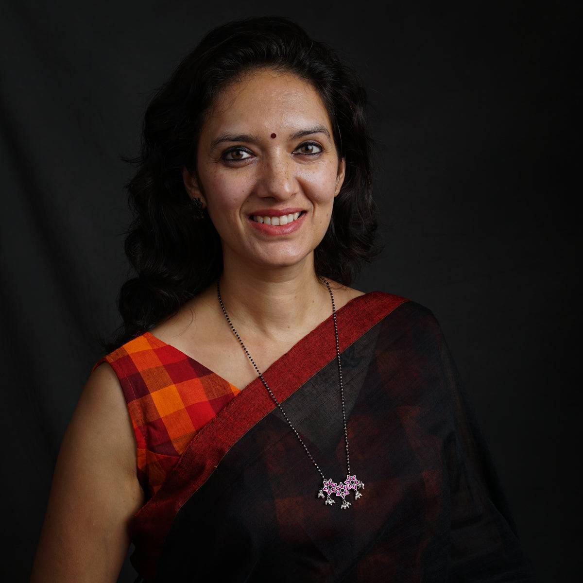 a woman in a red and black sari smiles at the camera